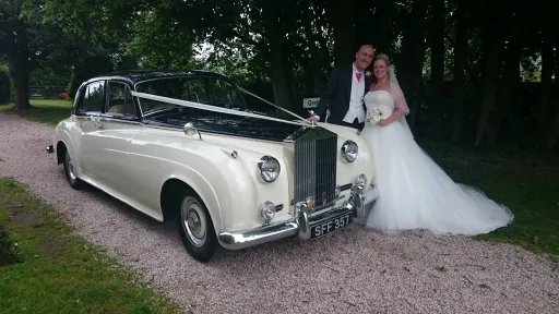Black & Ivory 60's Rolls-Royce Silver Cloud decorated with V-Shape White Ribbon with BRide and Groom Standing next to the car