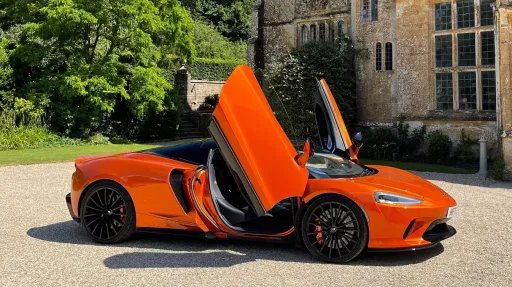 Burnt orange McLaren Wedding Car with doors open in front of wedding venue in Wiltshire