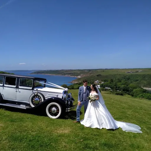 Bride and Groom next to the wedding car they've hired on top of a cliff in devon. Blue sea in background