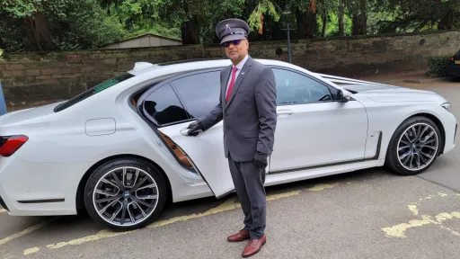 Right-Side View of White BMW with its chauffeur wearing silver suit and chauffeur's hat opening the door to his Norfolk wedding couple