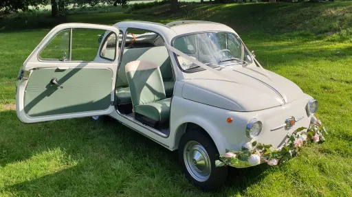Classic Italian Fiat 500 convertible with wide door open and garland of flowers on front bumper.