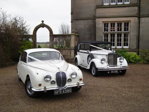 White Classic Jaguar Mk2 next to a Vintage Regent at a wedding venue in durham both deocrated with traditional V-Shape White Ribbon on the Bonnet