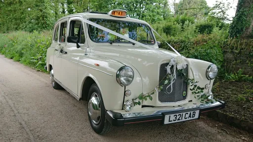Side view of Ivory Classic Taxi Cab in Cornwall with White Ribbons and flower decoration on front bonnet and old fashion Orange Taxi sign illuminated on Roof