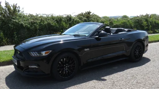 Side view of Black American Ford Mustang with roof open showing the black leather interio and black alloy wheels