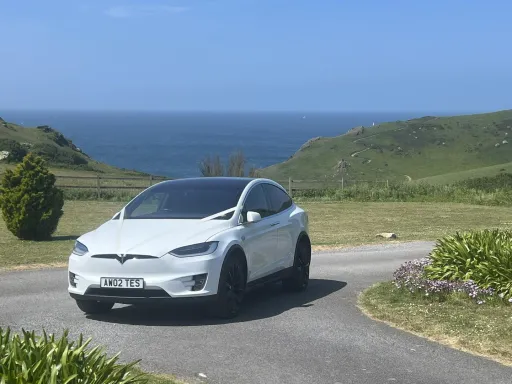 White Tesla on road by Devon southern coast  with spring flowers. Blue sea in Background