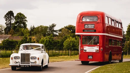 A Double Decker Routemaster Bus Leaving the Venue and a White Classic Rolls-Royce Entering the South Wales Wedding Venue. Both decorated with White Ribbons.