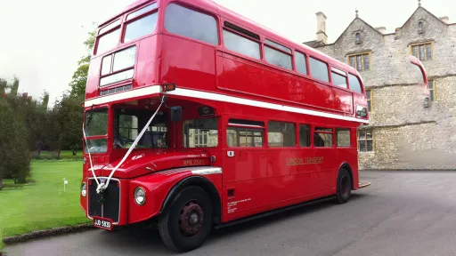 Vintage Double Decker Red Routemaster bus with White Ribbons at front leaving the wedding venue after dropping guests off