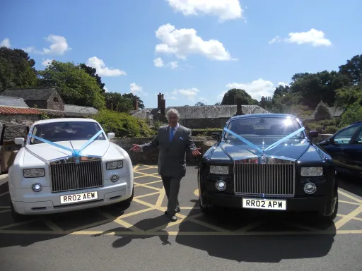 Two Rolls-Royce Phantom in Black and White decirated with Baby Blue Ribbons and Chauffeur standing in the middle of hte cars