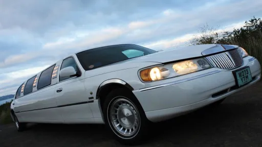 White Stretched Licoln Limousine at dusk with headlight and side light illuminated