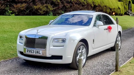Modern White Rolls-Royce Ghost with Red Bows on Door handles entering wedding venue in Carmarthenshire