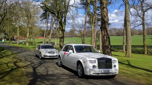 Modern White Rolls-Royce Phantom followed by a White Bentley Flying Spur both dressed with Red bow on the door handling driving through the long entrance at the  venue in Ceredigio