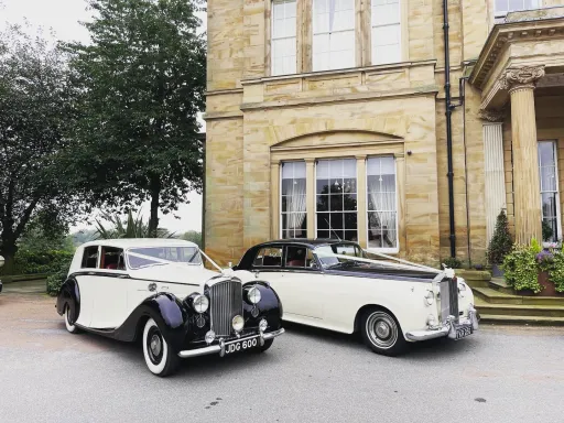Two Black & Ivory Classic Rolls-Royce decorated with white ribbons waiting for Bride and Groom in front of wedding venue in West Yorkshire