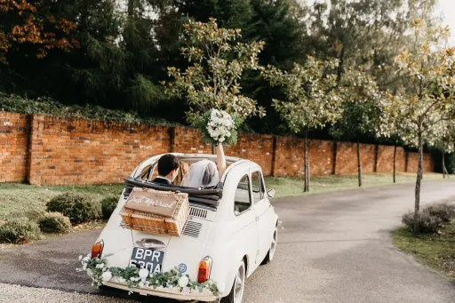 Rear view of Classic Convertible Fiat with roof open and "just Married" sign. Bride waving her bridal bouquet through the roof