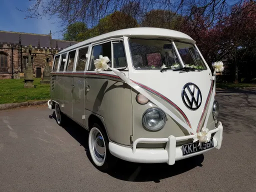 classic Vw Campervan in cream and white with white ribbons and white bows waiting for couple in front of venue in Derbyshire