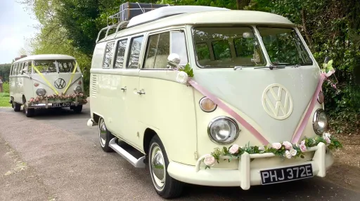 Two Matching Classic VW Campervans on wedding duties in Suffolk. Both campers are decorated with Pink Ribbons and flowers on front bumpers