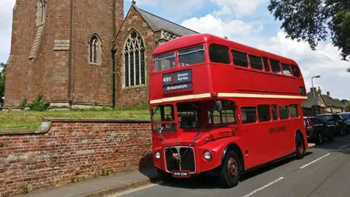 Side View of a Red Double Decker Routemaster Bus waiting in from of a church in Northamptonshire. Bus is decorated with Dark Blue Ribbons