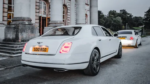 Rear view of a White Bentley Mulsanne with rear lights illuminated. A White rolls-Royce Ghost is standing in front of the Bentley