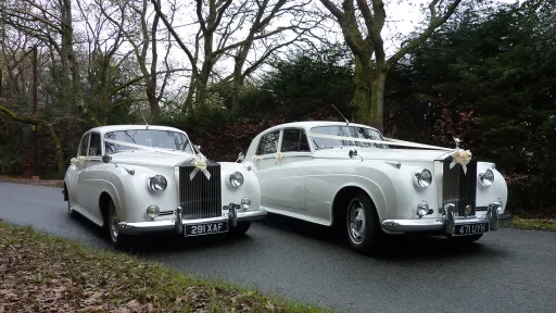 Two Matching White classic Rolls-Royce Wedding Car in Dorset Countryside . Both vehicles are standing side-by-side and decorated with white ribbons