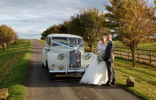 7-seater Classic Austin Princess Limousine with White Ribbon in West midlands Park with Bride and Groom standing in front of the vehicle