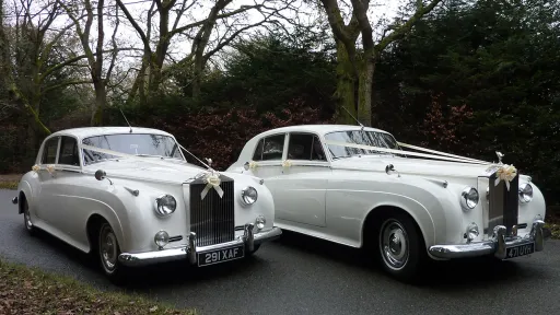 Two Rolls-Royce Silver Cloud decorated with White Ribbons and bows. Photo taken from the front showing the large imposing Rolls-Royce Grill