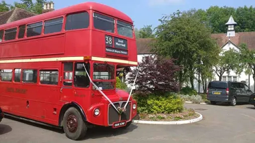 Double Decker Red Bus decorated with white ribbons outside wedding venue in Oxfordshire