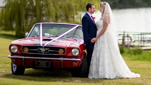 Red Convertible Ford Mustand decorated with White Ribbons with Bride and Groom next to the vehicle posing for photos