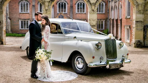 Classic 7-seater princess in Ivory decorated with white ribbons. Briode and Groom posing in front of the vehicle for photos with bride holding a bridal bouquet