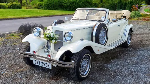 White vintage Beauford convertible decorated with Ivory Wedding Flowers on front grill