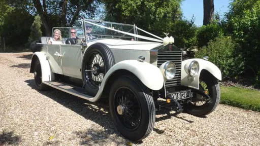 Vintage Rolls-Royce Convertible in front of weddingvenue in Dorset. Passengers seated in rear seat and car is decorated with White Ribbons