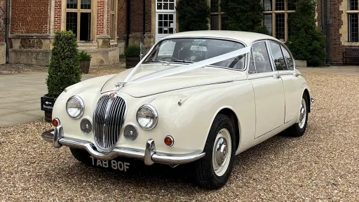 Ivory Classic Jaguar Mk2 hired in Hertfordshire. Car is outside the wedding venue dressed with white ribbons accross its bonnet
