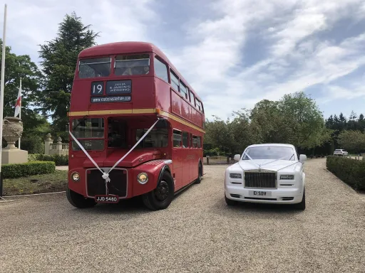 Red Double Decker Routemsster Bus on the Left and a White Rolls-Royce Phantom on the right bith decorated with ribbons waiting outside for bride and groom in Hertfordshire