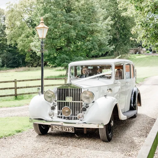 White vintage rolls-Royce Limousine entering Hampshire wedding venue with Bride and Groom. Car is decorated with white ribbons