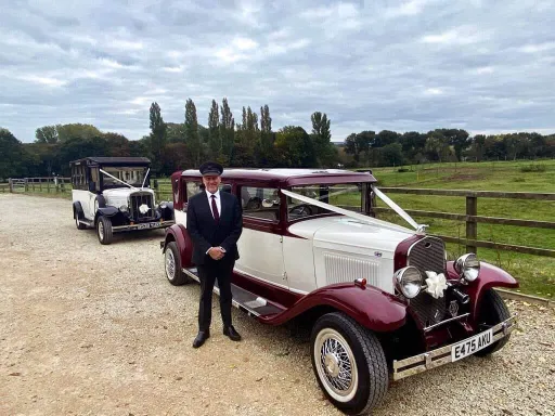 Two vintage cars with chauffeur standing by the vehicle. The first car at the front is Ivory and Burgundy and the second vehicle at the back is a vintage Asquith 8-seater bus in Bl