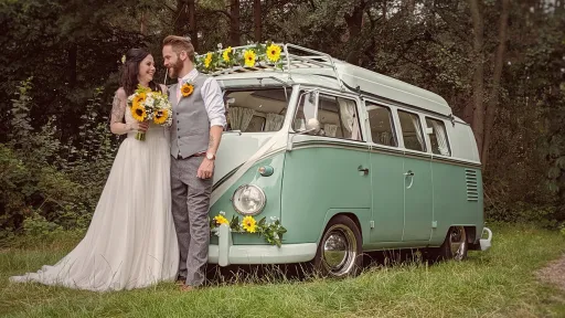 60's Campervan in green and White standing in a Park in Hampshire with bride and groom posing in fromnt of the vehicle. Vehicle is decorated with yellow sunflowers