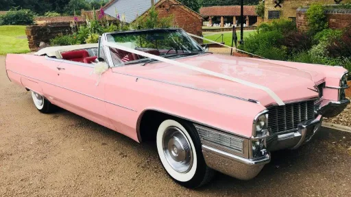 Classic American Pink Cadillac with white ribbons in front of wedding venue.