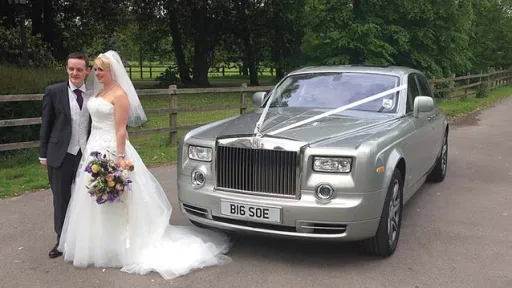 Silver Modern rolls-royce phantom dressed with white ribbons with bride and groom standing in front of the vehice. Bride is holding her bridal bouque in a right hand