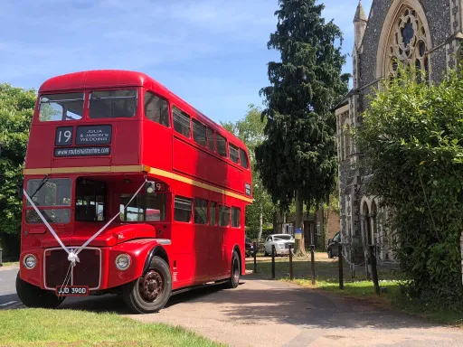 Vintage Red Routemaster bus standing ion from of church in London. White Ribbons at the front of the bus.