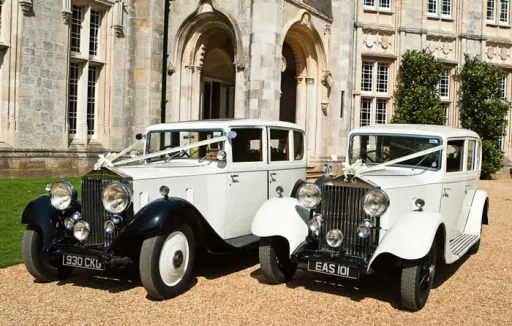 Two identical vintage rolls-royce in white with white traditional ribbons standing in front of Hampshire venue next to each others