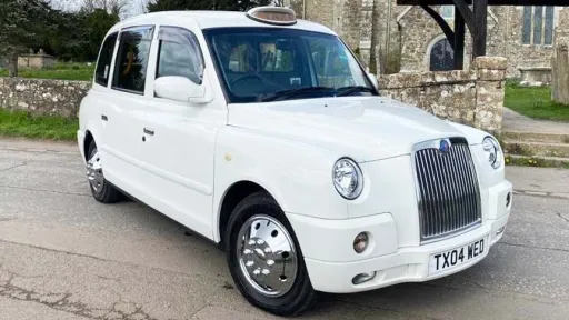 Side view of a modern White Taxi Cab with chrome alloy wheels in front of a church in East Yorkshire
