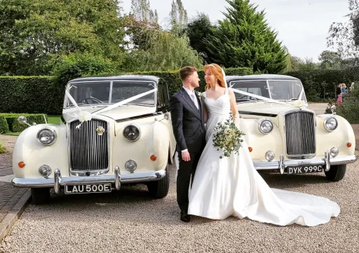 Two Matching Classic Austin Princess Limousine in front of Nottinghamshire Wedding Venue with Bride and Groom in the middle of the cars posing for photos