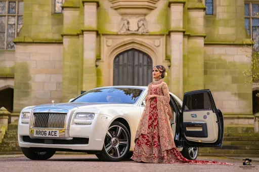 White rolls-Royce Ghost in front of wedding venue in Merseyside with Asian Bride dressed in Red Wedding Dress standing by the car