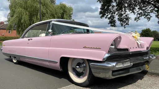 Side view of Pink Cadillac howing white wall tires and white wedding ribbons accross its bonner