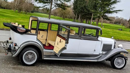 Two Tone White and Bronze 7-seater Bramwith Limosuine with rear door open showing the cream leather seats and burgundy carpet inside the rear cabin. The roof is open.