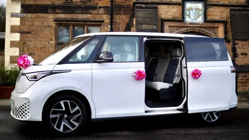 White Electric VW Campervan with pink Bows. Door is open whoing the light blue and white interior