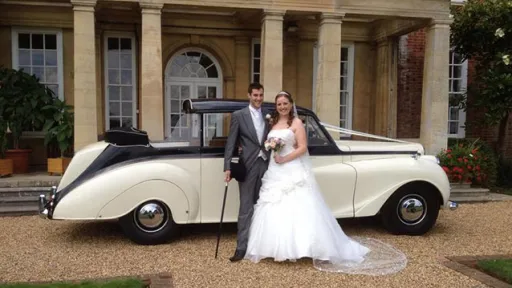 Convertible Classic Austin Limousine in Black & ivoryu in fronf ot venue in Nottinghamshire with Bride and Groom posing for photos in front of the vehicle