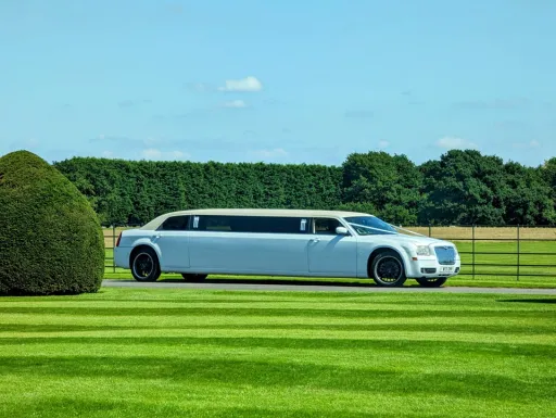 White Stretched Limousine entering wedding venue. Limousine has blacked out windows, black alloy wheels and decorated with White Ribbons