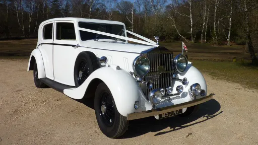 White Vintage Rolls-Royce showing the 1930's style headlamps and large imposing Rolls-Royce grill