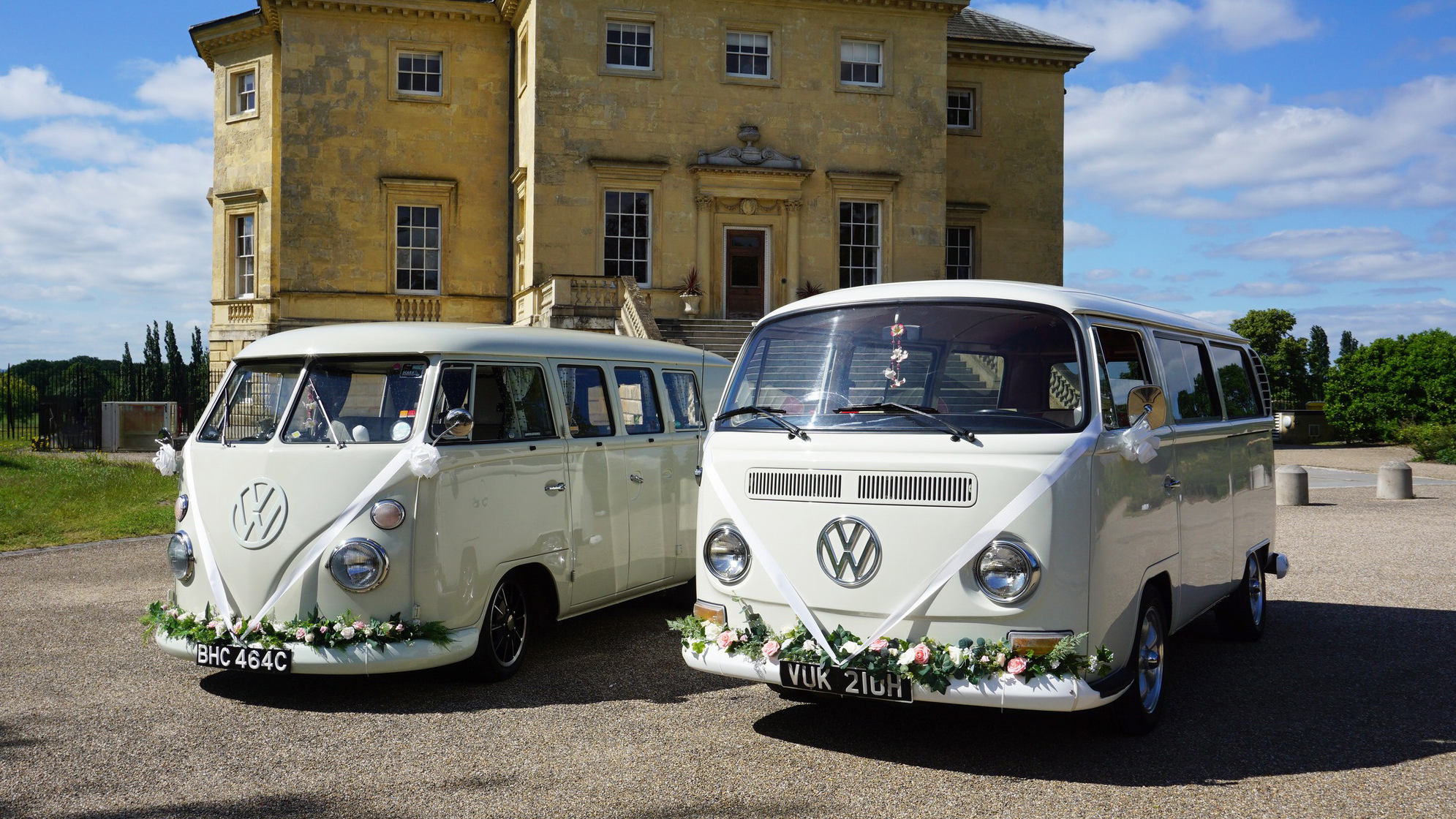 Two Classic VW Campervans decorated with a green foliage arrangement on front bumpers and white ribbons across the front
