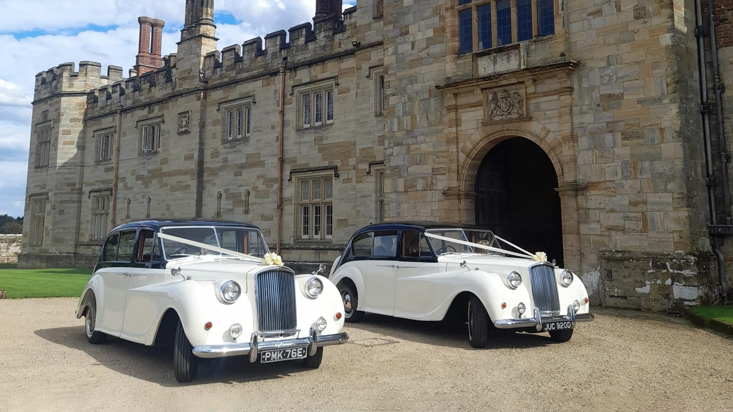 Two Classic Austin Princess Limousine decorated with Ivory Ribbons and Bows on top of the front grill. Vehicles are parked in front of a large manor house in Maidstone