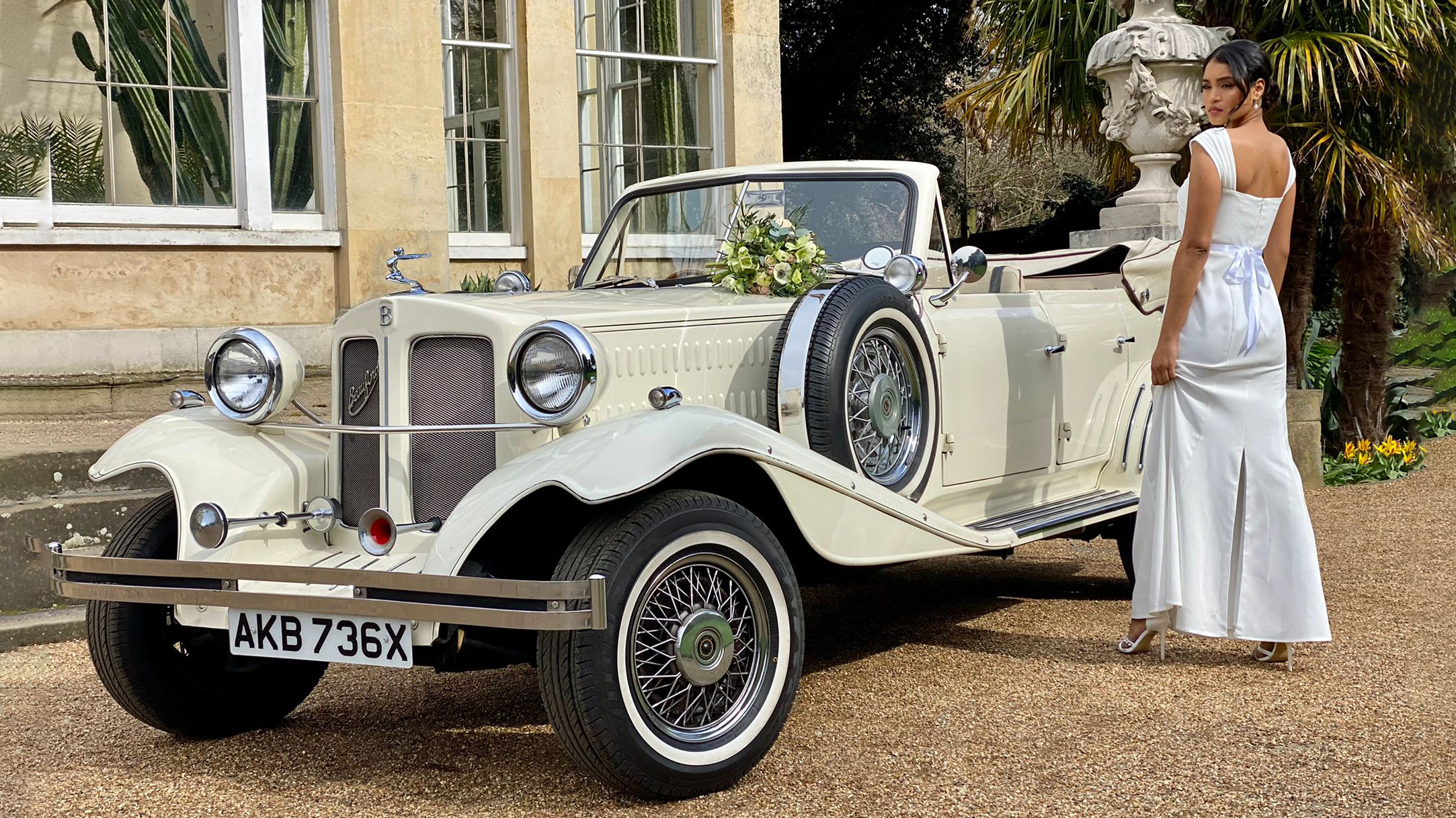 Vintage Ivory Beauford with roof down and spare mounted wheel on the side of the vehicle with bride standing by the car wearing a white dress